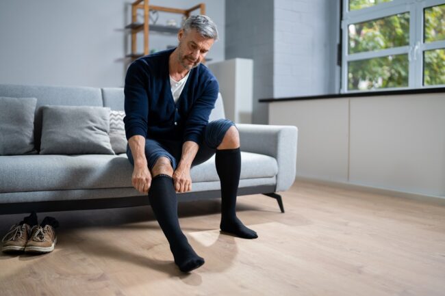 Man pulling on a compression sock to alleviate discomfort after varicose vein treatment