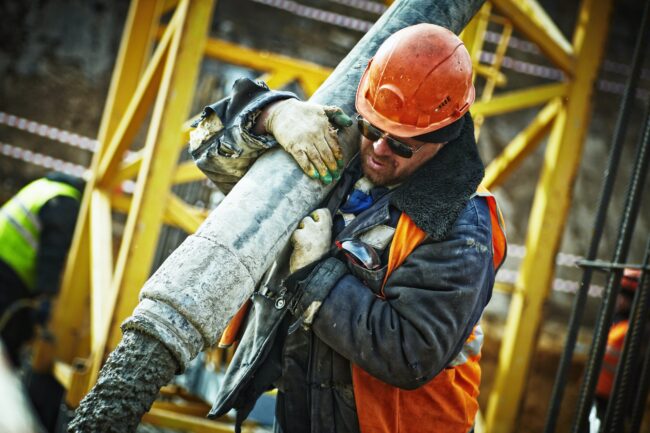Construction worker in a hard hat lifting up a heavy pipe