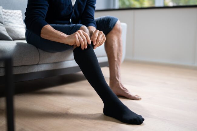 Man putting on medical compression stockings, one of the ways to keep veins safe during strenuous sports and activities