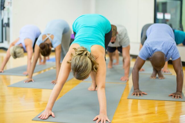 People doing the downward dog pose in a yoga studio. This stretch targets the hamstrings and calf, making a great option for alleviating varicose vein symptoms